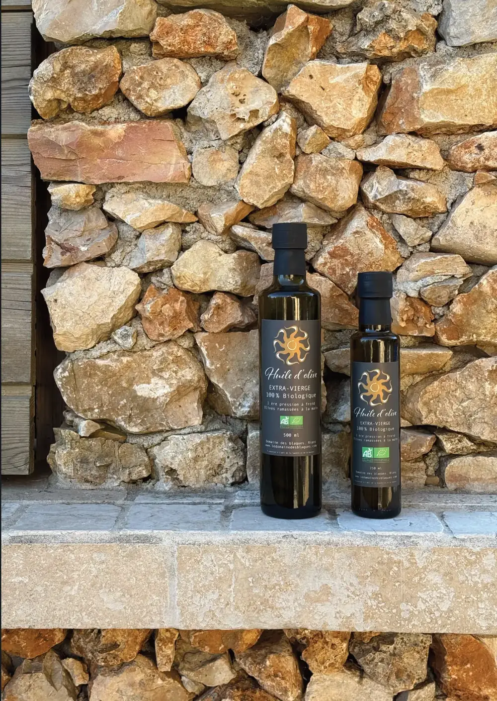 Bouteilles d’huile d’olive devant un mur de pierres sèches